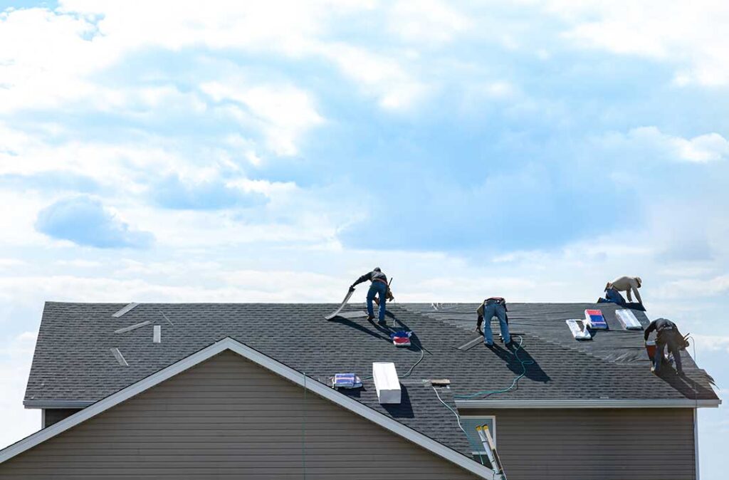 A roofer inspects metal flashing around a plumbing vent on a shingled roof.